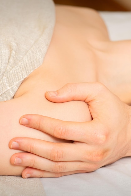 Male masseur massaging shoulder of a young woman lying on a massage table in a spa clinic.