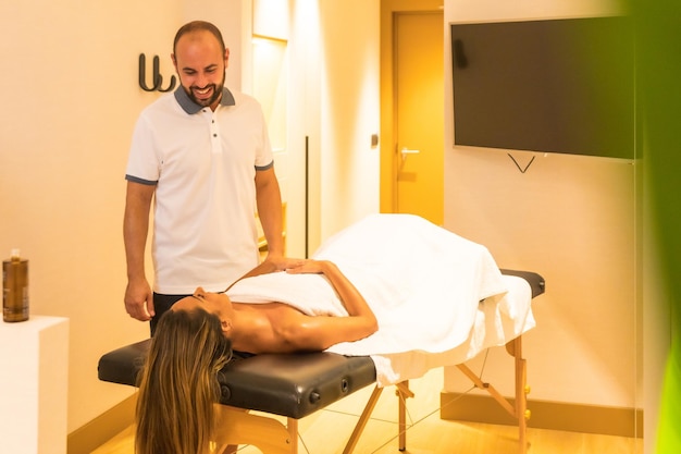 Male masseur performing a massage on the stretcher to a female client and explaining the treatment