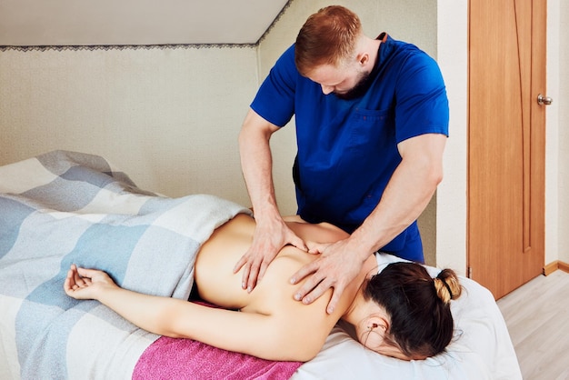 Массажист-мужчина сильно нажимает обеими ладонями на мышцы спины женщины, когда он дает глубокий массаж