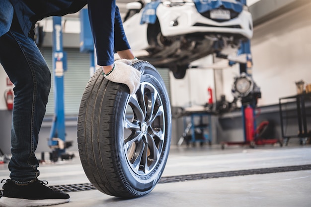 Male mechanic hold and rolling tire at repairing service garage background