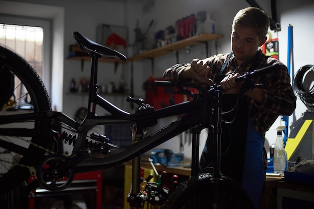 Foto meccanico maschio che fa servizio nel negozio di riparazione di biciclette utilizzando strumenti