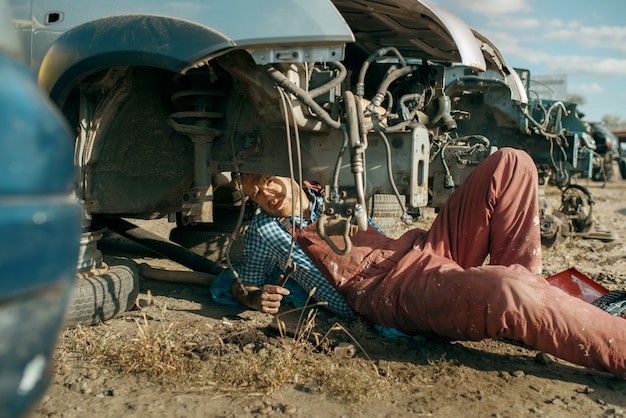 Male mechanic in welding glasses on car junkyard