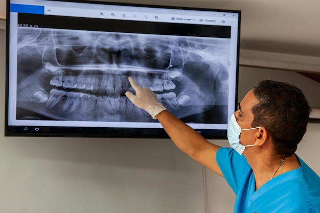 Male middle -aged dentist at his office using an x ray image to explain treatment to his patient