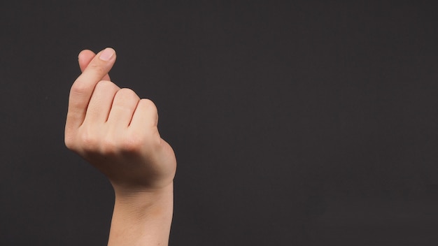 Male model is doing mini heart hand sign on black background.