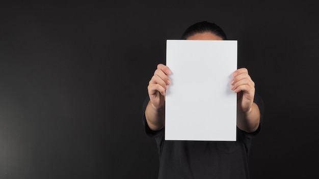 Фото Руки мужской модели держат чистый лист бумаги формата а4 на черном фоне.