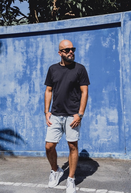 Male model with beard wearing black blank tshirt on the background of an blue wall