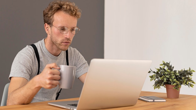 Мужская модель работает на своем ноутбуке и пьет кофе