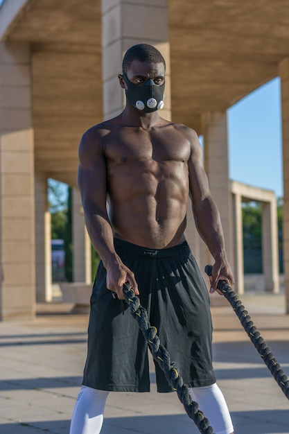 Male muscular training with battle ropes and training mask 