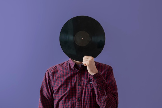 A male music lover holding a black vinyl record and cover his face