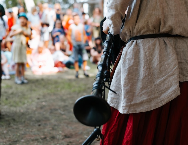 Un musicista maschio in un costume medievale che tiene un vecchio strumento tradizionale a cornamusa concerto folk all'aperto vista posteriore del primo piano