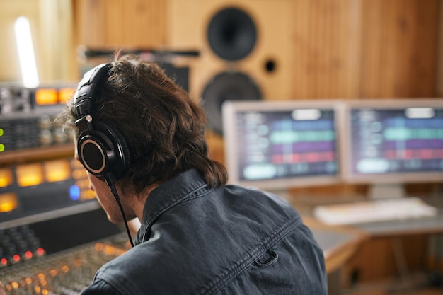 Male musician wearing headphones at audio workstation in professional recording studio copy space