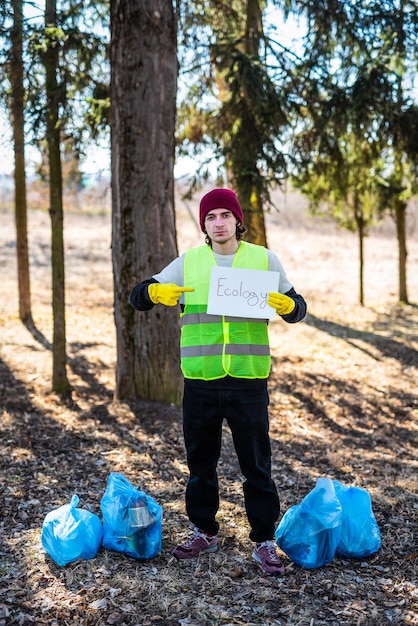 Male nature activist holds white template paper while standing\
near blue trash bags