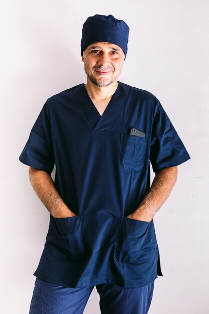 Male nurse, doctor or vet in blue uniform at a window in a hospital, hands in pockets, smiling. Medicine, hospital and healthcare concept.