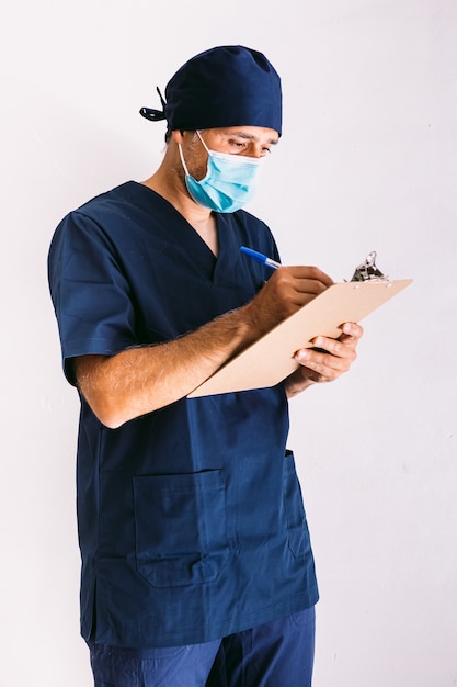 파란색 제복을 입은 남자 간호사, 의사 또는 수의사는 파란색 마스크를 쓰고 병원 창가에서 보고서를 작성합니다. 의학, 병원 및 의료 개념입니다.