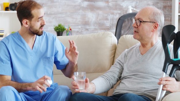 Male nurse giving pills to retired man in nursing home.