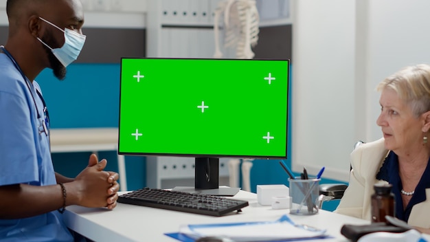 Медсестра-мужчина и пациент в инвалидной коляске смотрят на зеленый экран на мониторе, изолированный дисплей. Мужчина и пожилая парализованная женщина используют шаблон макета хромакея с пустым фоном copyspace.