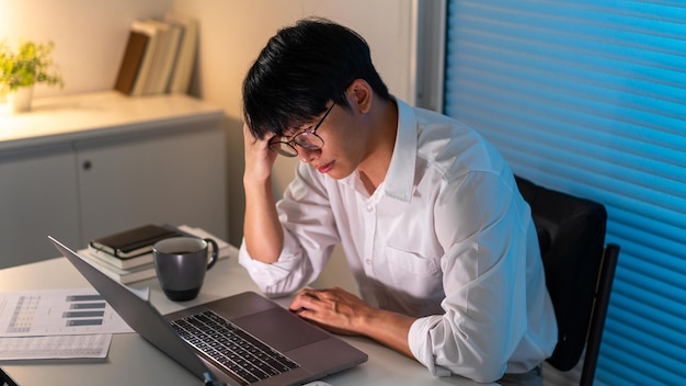 The male officer resting his forehead on his right hand while working late at his desk