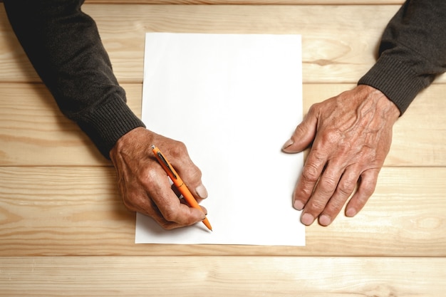 Photo male old hands writes on a blank sheet of paper