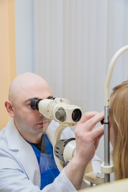 A male ophthalmologist checks the eyesight of a young girl using a modern device with a light beam