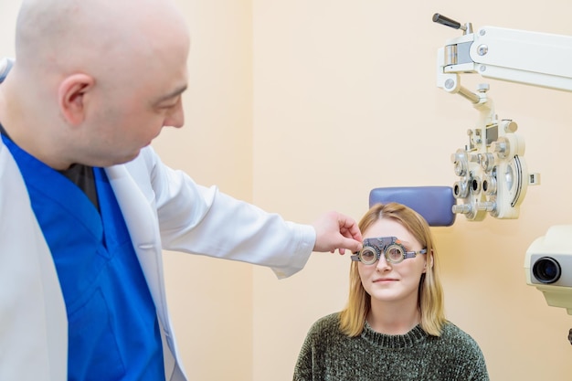 A male optometrist checks the eyesight of a young girl with a trial frame