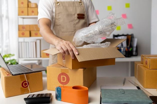 Male owner of an online store packs products into parcel boxes based on orders from online sales sites packs products for delivery to addresses via private courier service Product packaging concept