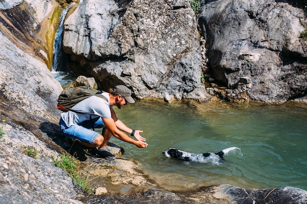 Male owner of spaniel dog walking against mountains and waterfall background