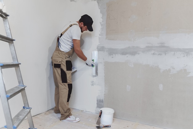 Художник-мужчина со шпателем в руках делает ремонт дома. Концепция ремонта номеров.