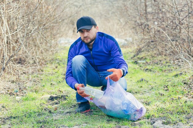 Male park worker collects garbage and plastic in the forest in the spring takes care of the ground and trees