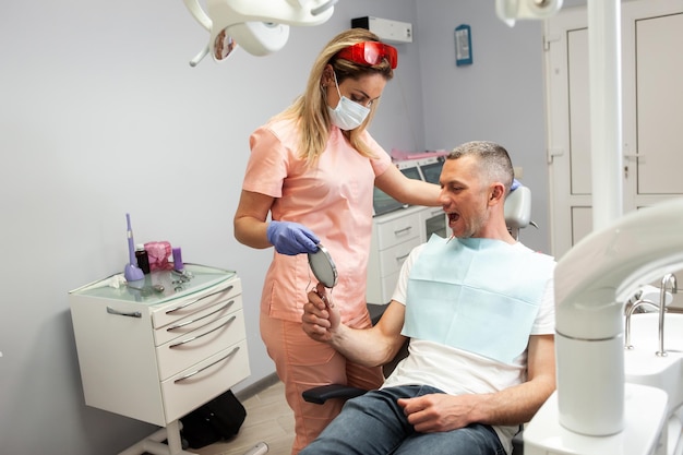 Пациент-мужчина осматривает свои зубы в зеркале у стоматолога в стоматологической клинике Посещение стоматолога Стоматологическое лечение