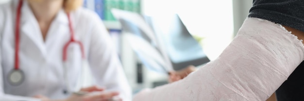 Пациент мужского пола с повязкой на руке сидит на приеме у травматолога крупным планом
