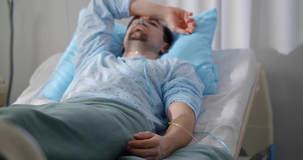 Male patient with iv drip on hand lying in bed at hospital ward