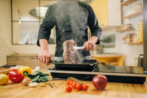 Male person cooking meat in a pan on the kitchen