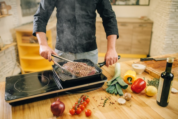 Male person cooking meat in a pan on the kitchen.