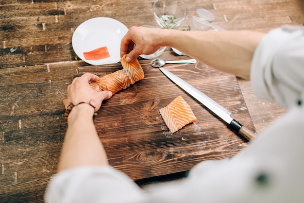 Male person cooking seafood on wooden table, japanese kitchen preparation process. Traditional asian cuisine, sushi making