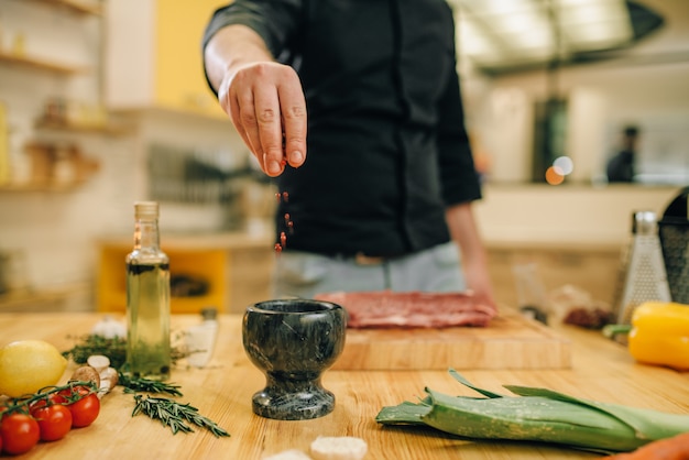 Male person marinating raw meat on wooden board. Chef cooking tenderloin with vegetables, spices and herbs