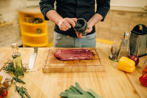 Male person sprinkles raw meat with seasonings