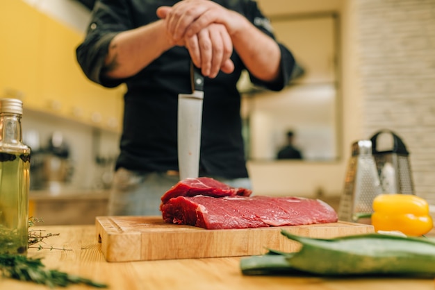 Фото Мужчина с ножом и куском сырого мяса на деревянной доске