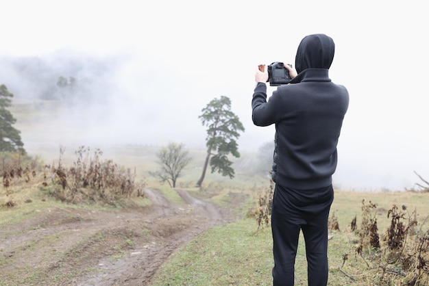 泥だらけの道で霧の秋の風景の写真を撮る男性カメラマン