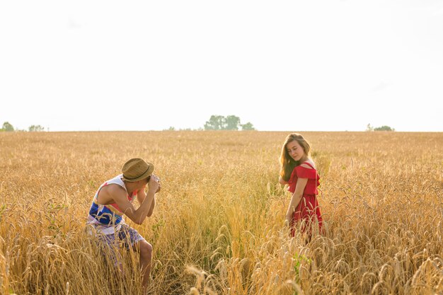 Male photographer taking pictures of a young woman standing in field. Couple enjoying day on nature