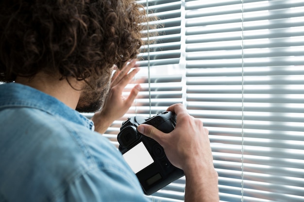 Мужской фотограф с цифровой камерой, глядя через жалюзи