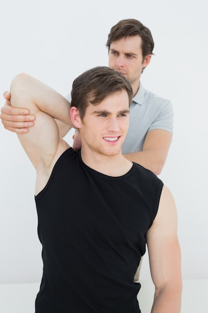 Male physiotherapist stretching a smiling young mans arm