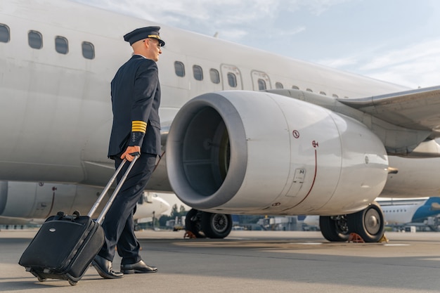 Male pilot walking along commercial airplane outdoors