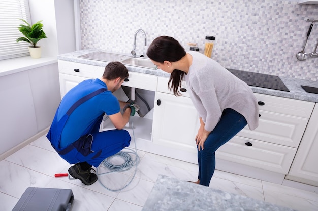 Male plumber cleaning clogged sink pipe with drained cable