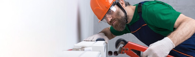 A male plumber installs a radiator in the heating system of an apartment Guy in overalls and a gas wrench