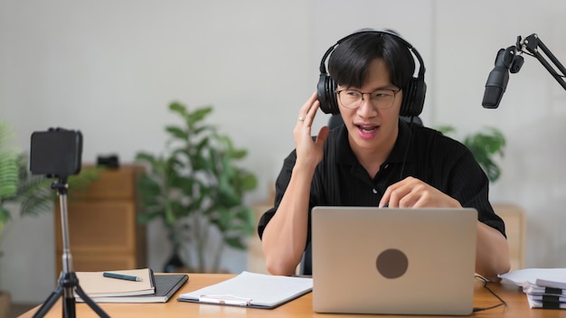 Male podcaster use laptop and speaking on microphone to recording audio podcast in broadcast studio