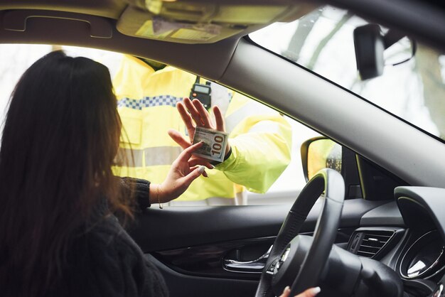 Male police officer in green uniform refuse to take bribe from woman in vehicle.