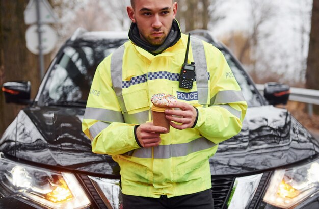 Male police officer in green uniform taking a break with donut on the road.