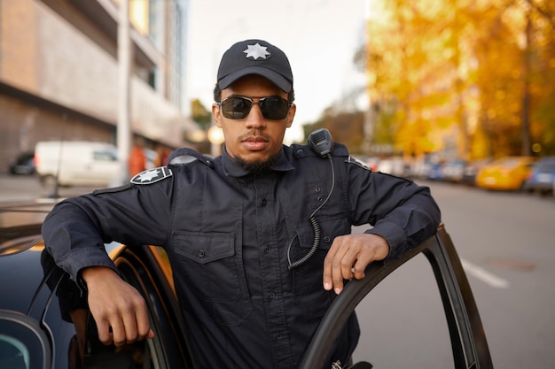 Male police officer in uniform poses at the patrol car. Policeman protect the law. Cop works on city street, order and justice control