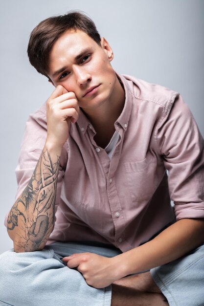 Male portrait on a gray background. A young guy in blue jeans and a shirt on a gray background