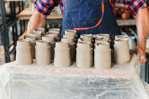 Male potter hands holding tray with ceramic pots in the pottery.